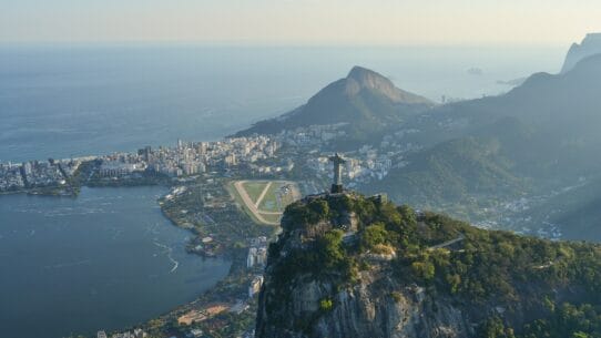 Drone view of Christ the Redeemer overlooking Rio de Janeiro, Brazil, with Rodrigo de Freitas Lagoon, mountains, and the Atlantic Ocean in the background.