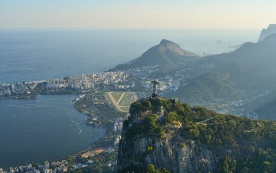 Drone view of Christ the Redeemer overlooking Rio de Janeiro, Brazil, with Rodrigo de Freitas Lagoon, mountains, and the Atlantic Ocean in the background.