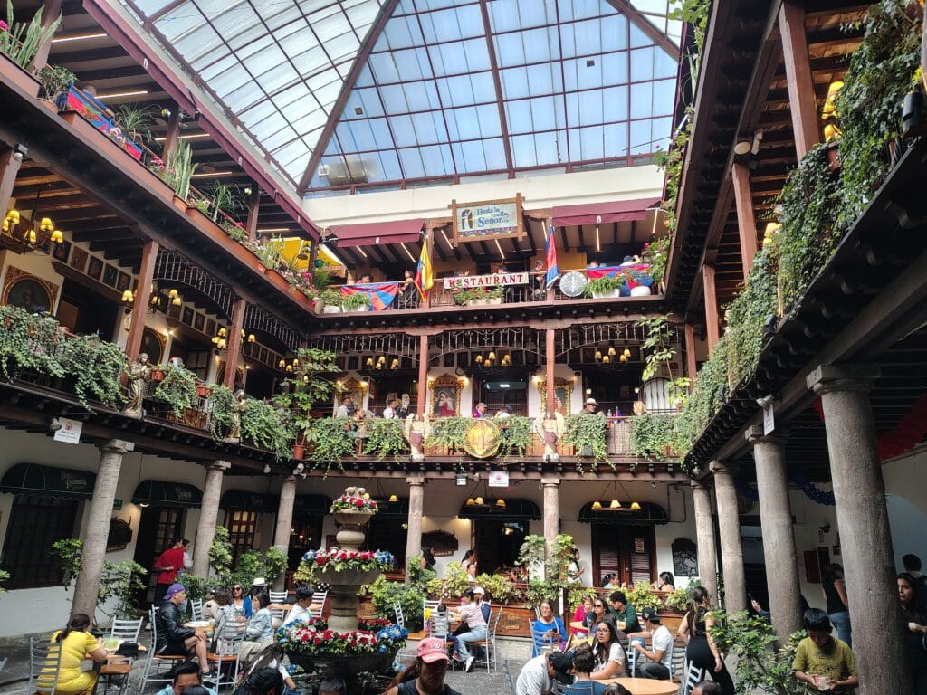 nterior courtyard of a traditional colonial building with restaurants, balconies, plants, and outdoor seating in Quito.