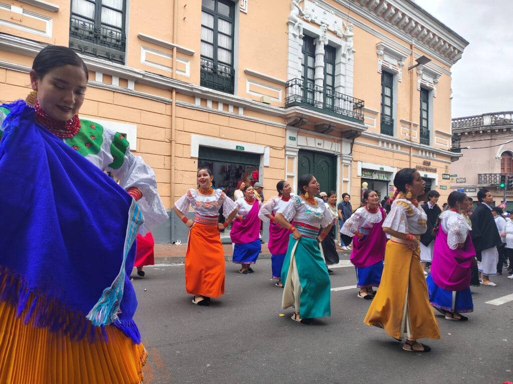 Women wearing colorful traditional dresses performing during the Fiestas de Quito parade in Ecuador.