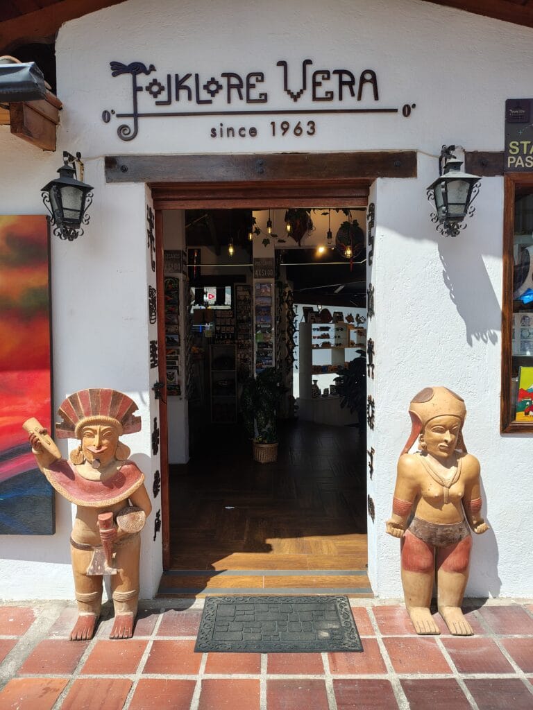 Entrance to the Folkore Vera artisan shop at Ciudad Mitad del Mundo in Ecuador, featuring traditional Indigenous-inspired sculptures and handcrafted souvenirs.