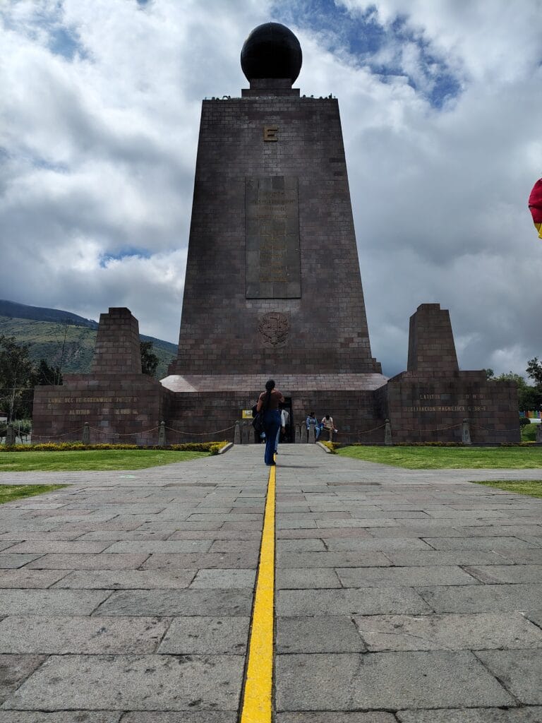 The Mitad del Mundo Monument in Ecuador with the symbolic yellow Equator line leading directly to the entrance under dramatic Andean skies.