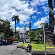 Plaza Grande in Quito, Ecuador, with the Independence Monument, colonial buildings, and directional signs pointing to major attractions.