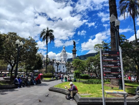 Plaza Grande in Quito, Ecuador, with the Independence Monument, colonial buildings, and directional signs pointing to major attractions.