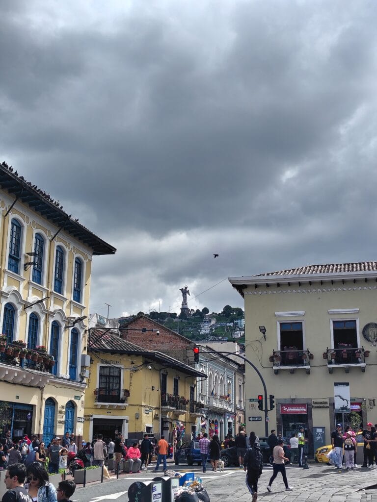 Colonial street in Quito with the Virgin of El Panecillo monument visible on the hill in the distance.