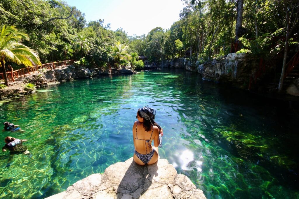 Traveler sitting beside a crystal-clear cenote surrounded by tropical forest in Mexico.