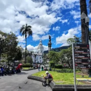 Plaza Grande, em Quito, no Equador, com o Monumento à Independência, edifícios coloniais e placas indicando as principais atrações.